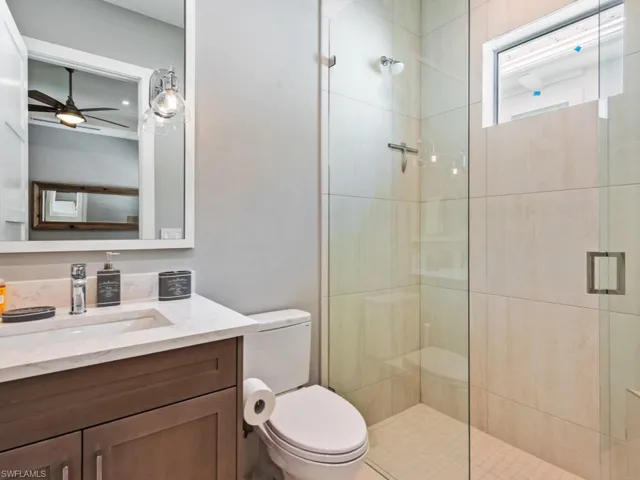 Bathroom with a shower with door, vanity, ceiling fan, and toilet