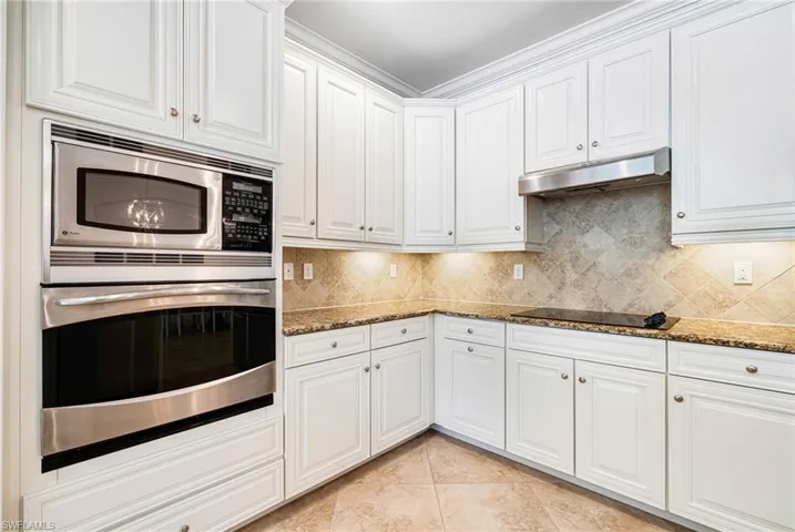 Kitchen with crown molding, white cabinets, stainless steel appliances, and dark stone countertops