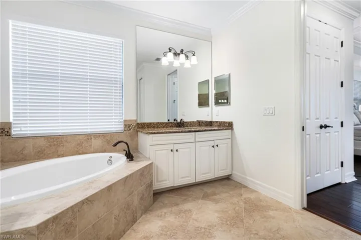 Bathroom with vanity, crown molding, and tiled bath