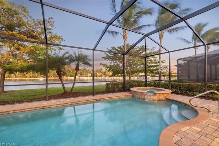 Pool at dusk featuring an in ground hot tub, a water view, and glass enclosure