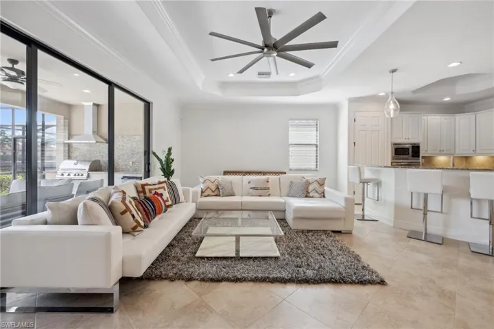 Living room featuring crown molding, ceiling fan, a raised ceiling, and a wealth of natural light