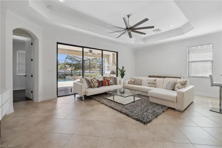 Tiled living room featuring ceiling fan, ornamental molding, and a tray ceiling