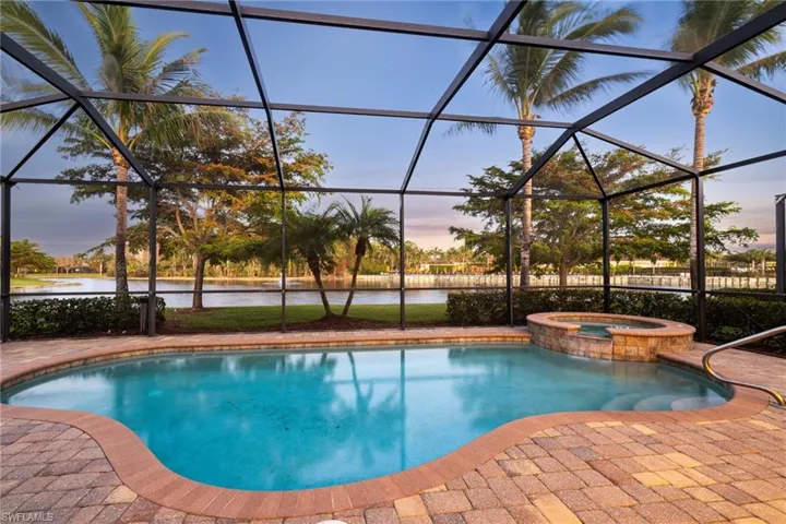Pool at dusk with a patio area, an in ground hot tub, a water view, and glass enclosure