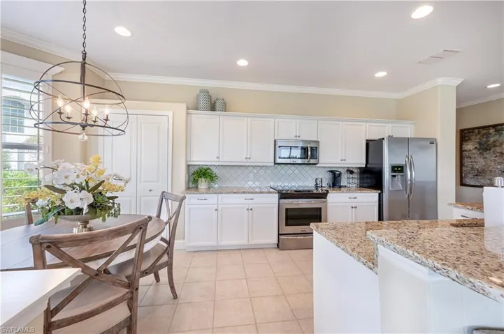 Kitchen with white cabinets, decorative light fixtures, an inviting chandelier, appliances with stainless steel finishes, and light stone counters