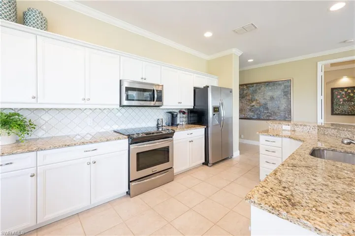 Kitchen featuring tasteful backsplash, light stone countertops, appliances with stainless steel finishes, sink, and white cabinetry