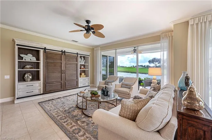 Living room with ceiling fan, ornamental molding, light tile patterned floors, and a barn door