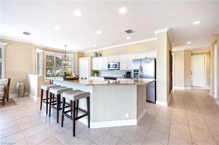 Kitchen with white cabinets, an island with sink, appliances with stainless steel finishes, ornamental molding, and light stone counters