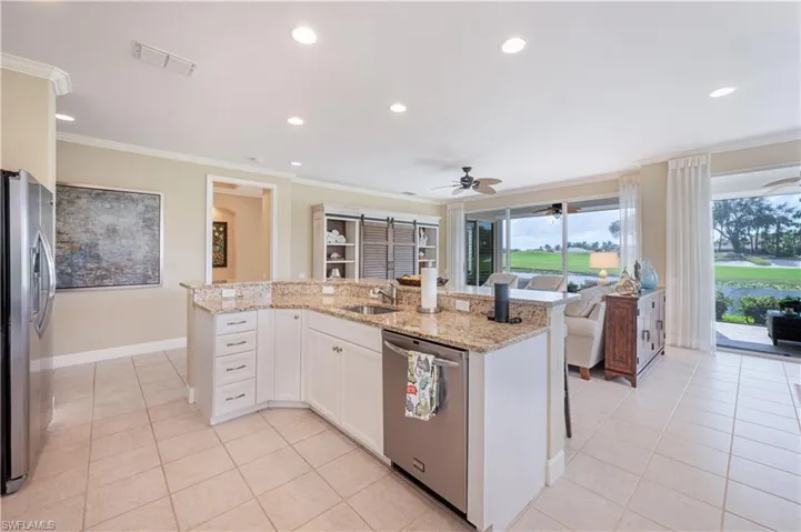 Kitchen featuring stainless steel appliances, ornamental molding, a barn door, white cabinetry, and light stone counters