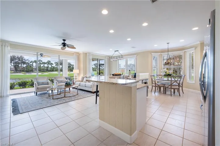 Kitchen featuring an island with sink, stainless steel fridge, pendant lighting, crown molding, and light tile patterned floors