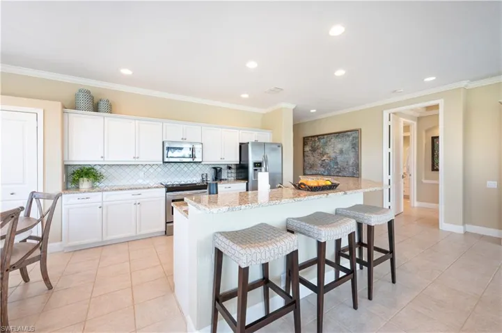 Kitchen with white cabinetry, a kitchen island with sink, stainless steel appliances, and light stone counters