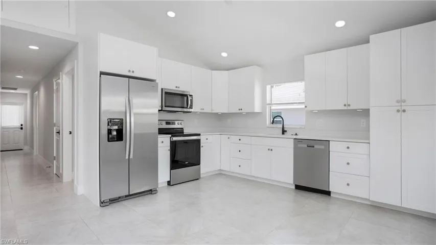 Kitchen featuring appliances with stainless steel finishes, light countertops, a sink, vaulted ceiling, and white cabinets