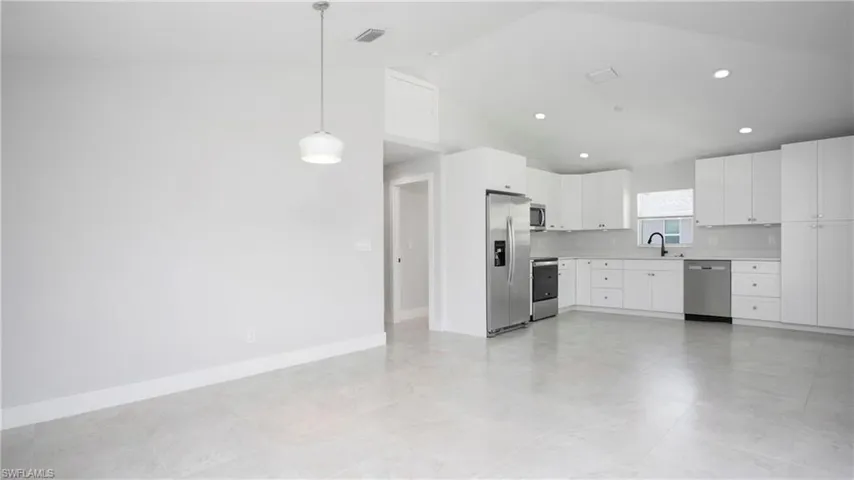 Kitchen featuring stainless steel appliances, a sink, light countertops, white cabinetry, and hanging light fixtures