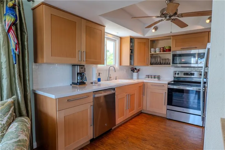Kitchen with stainless steel appliances, tasteful backsplash, wood finished floors, light countertops, and a ceiling fan