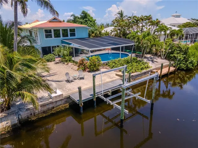 Back of house with boat lift, a water view, an outdoor pool, glass enclosure, and a patio