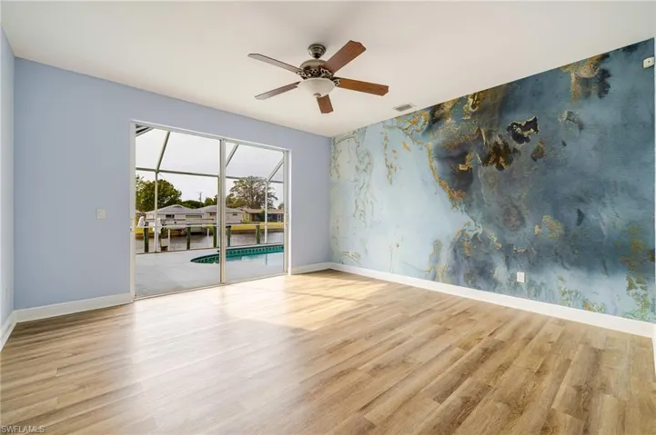 Empty room featuring an accent wall, ceiling fan, light wood-style flooring, a sunroom, and wallpapered walls