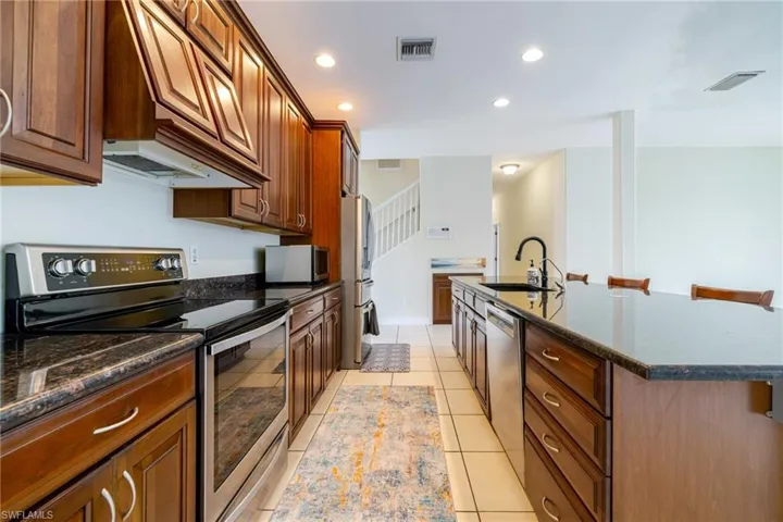 Kitchen featuring stainless steel appliances, dark stone countertops, recessed lighting, an island with sink, and a kitchen breakfast bar