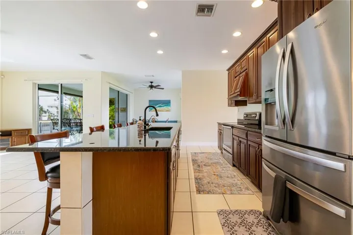 Kitchen with stainless steel appliances, a kitchen bar, recessed lighting, a kitchen island with sink, and dark stone countertops
