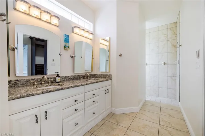 Full bath featuring double vanity, light tile patterned floors, and a walk in shower