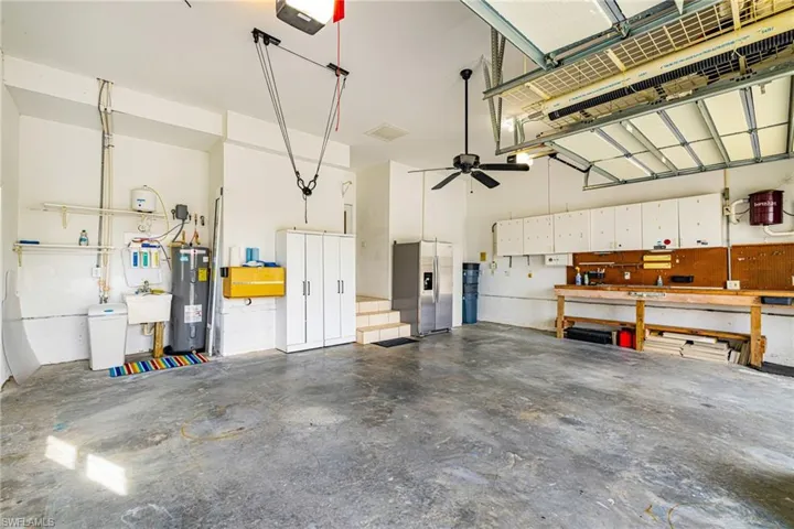 Garage with stainless steel refrigerator with ice dispenser, electric water heater, a garage door opener, and a workshop area