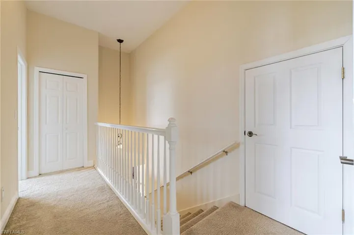 Hallway featuring light colored carpet and an upstairs landing