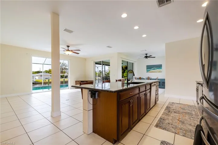 Kitchen with open floor plan, a center island with sink, freestanding refrigerator, light tile patterned floors, and recessed lighting