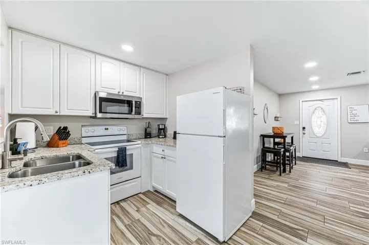 Kitchen featuring light stone counters, sink, white cabinets, and white appliances