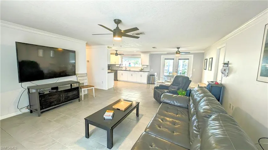 Living room with a textured ceiling, ceiling fan, crown molding, and light tile floors