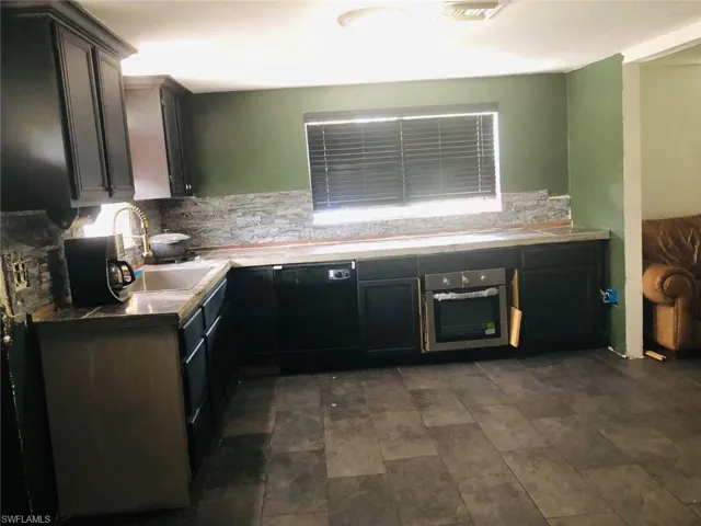 Kitchen with dark tile floors, backsplash, oven, dishwasher, and sink
