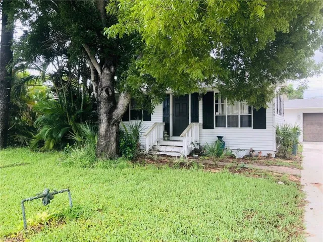 View of property hidden behind natural elements with a garage and a front yard