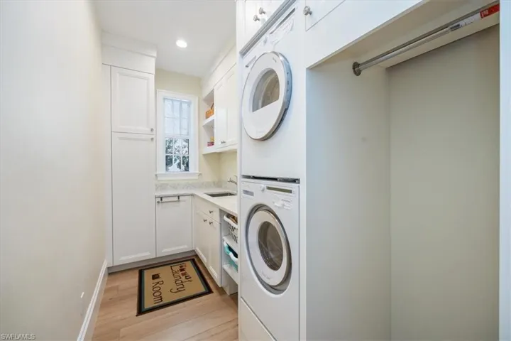 Washroom with sink, cabinets, stacked washer and clothes dryer, and light hardwood / wood-style floors
