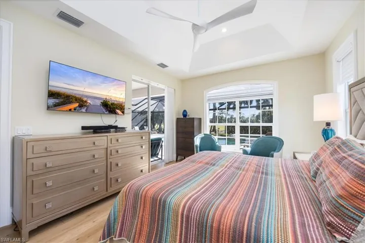 Bedroom with ceiling fan, a tray ceiling, and light hardwood / wood-style flooring
