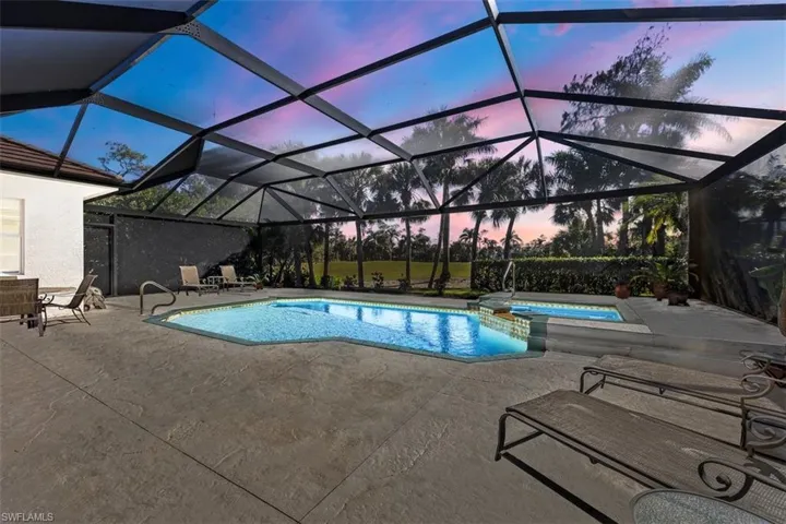 Pool at dusk featuring an in ground hot tub, a patio, and glass enclosure