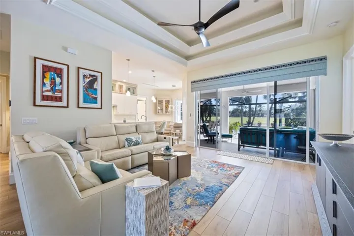 Living room with ceiling fan, a raised ceiling, and light wood-type flooring