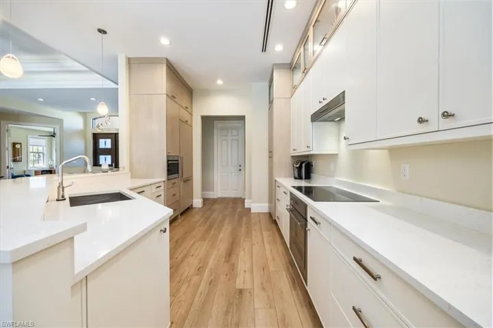 Kitchen with light stone countertops, sink, pendant lighting, light hardwood / wood-style floors, and appliances with stainless steel finishes