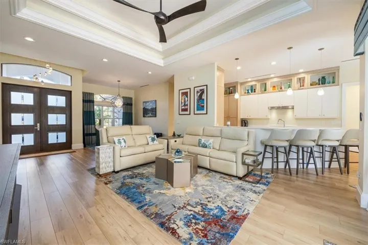 Living room featuring ceiling fan with notable chandelier, light wood-type flooring, ornamental molding, and a tray ceiling