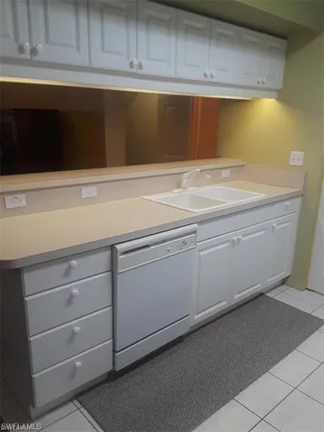 Kitchen with sink, white cabinetry, tile patterned floors, and dishwasher