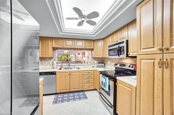 Kitchen featuring a ceiling fan, appliances with stainless steel finishes, light countertops, light tile patterned floors, and ornamental molding