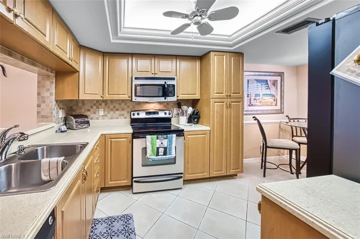 Kitchen featuring stainless steel appliances, light countertops, a tray ceiling, ceiling fan, and crown molding