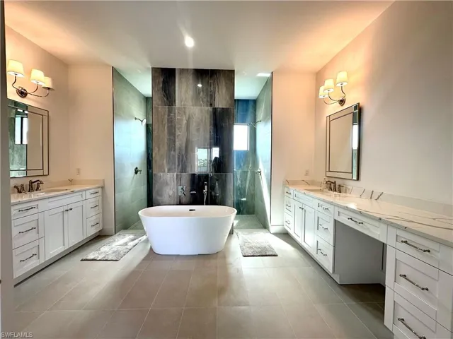 Full bath featuring a walk in shower, a freestanding tub, two vanities, and tile walls