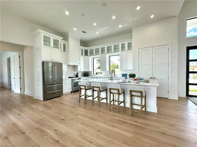 Kitchen featuring high quality appliances, white cabinets, a kitchen bar, a kitchen island with sink, and glass fronted cabinets