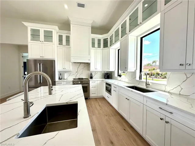 Kitchen with light stone counters, premium appliances, white cabinetry, tasteful backsplash, and light wood finished floors