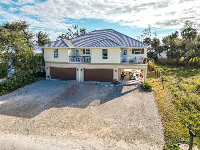 Coastal home featuring driveway, a balcony, a metal roof, and an attached garage