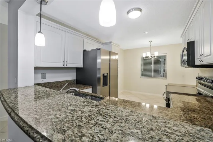 Kitchen with dark stone countertops, light tile patterned floors, a sink, white cabinetry, and stainless steel appliances
