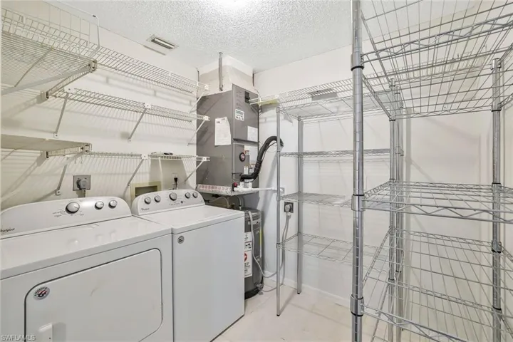 Clothes washing area featuring visible vents, heating unit, laundry area, a textured ceiling, and washing machine and clothes dryer