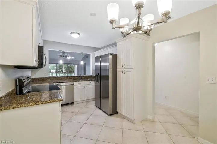 Kitchen with light tile patterned floors, an inviting chandelier, a sink, white cabinetry, and stainless steel appliances