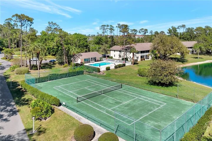 View of sport court featuring fence, a lawn, and a water view