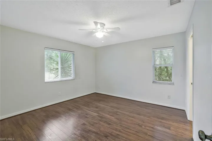 Spare room with a healthy amount of sunlight, dark wood-style flooring, visible vents, and ceiling fan