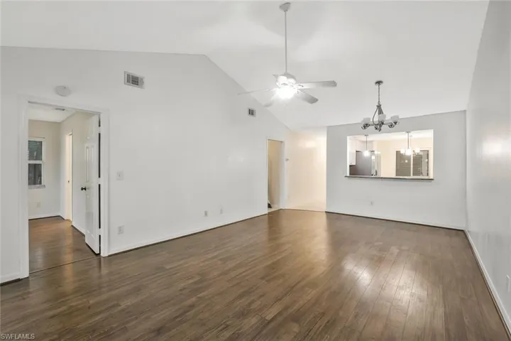 Unfurnished room featuring high vaulted ceiling, visible vents, ceiling fan with notable chandelier, and dark wood finished floors