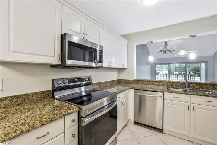 Kitchen featuring a sink, appliances with stainless steel finishes, white cabinetry, dark stone counters, and light tile patterned flooring