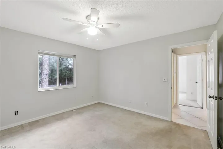 Empty room with light carpet, ceiling fan, light tile patterned floors, and a textured ceiling